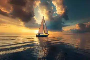 A sailboat floating on a calm sea at sunset