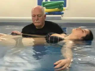 Man helping a woman float in a pool for aquatic therapy